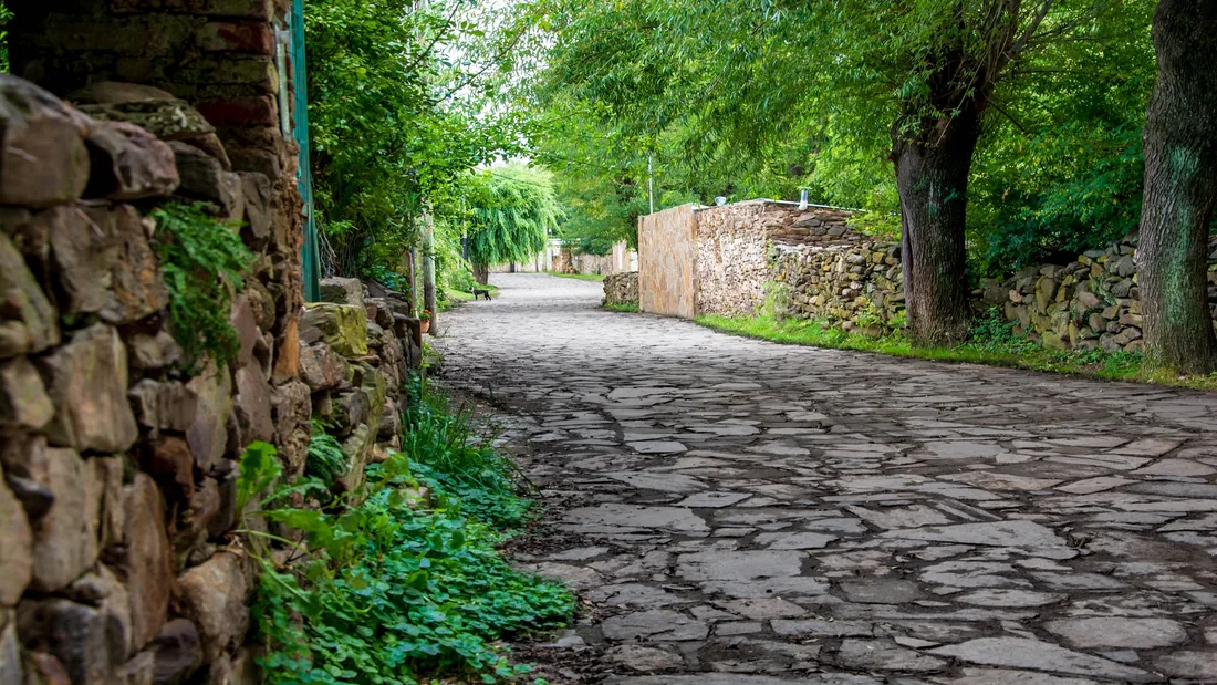 Calle de piedra del pueblo de La Carolina, entre árboles y muros de piedra